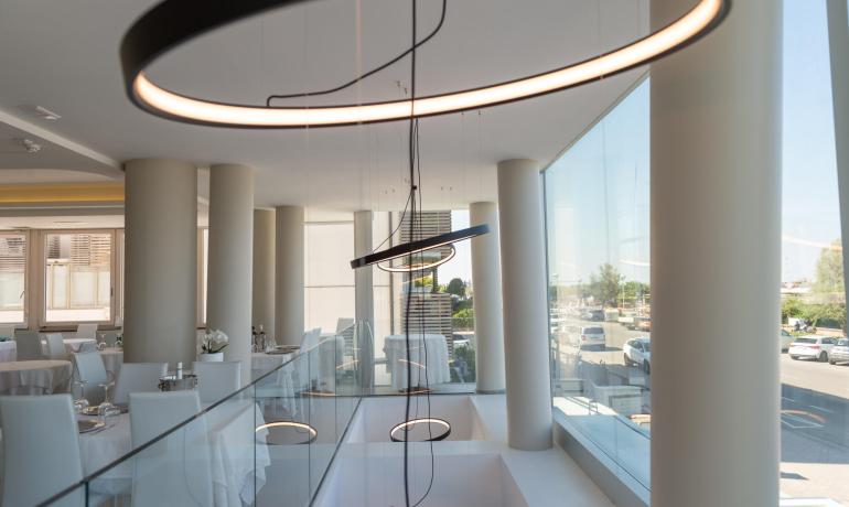 Ristorante moderno con lampade ad anello e ampie vetrate.