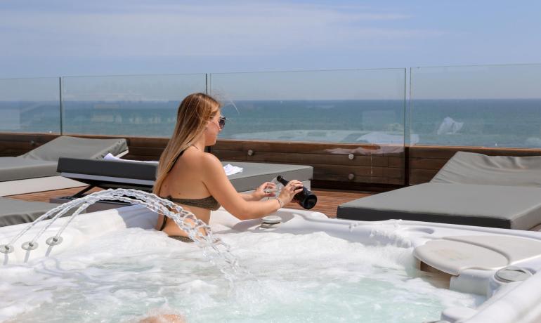 Donna in jacuzzi con vista mare, versa da una bottiglia.