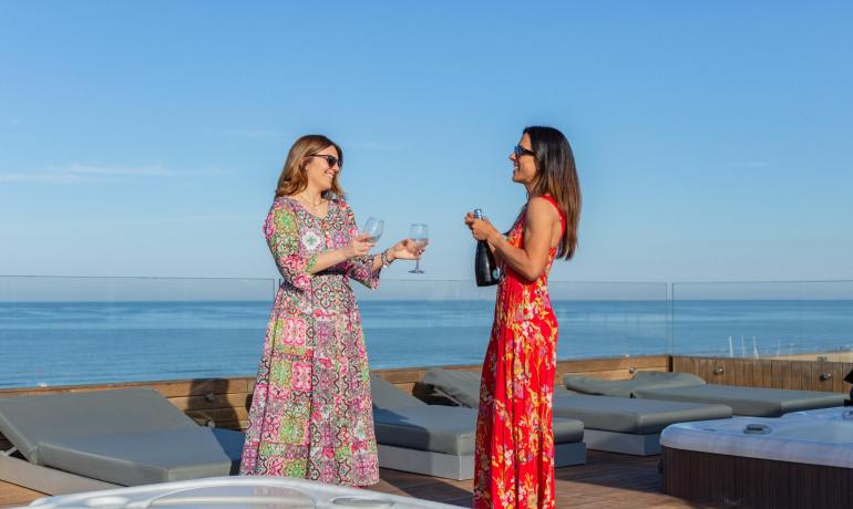 Due donne brindano su una terrazza con vista mare.