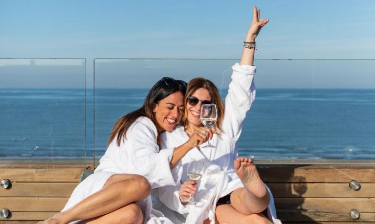 Due donne felici brindano in accappatoio su una terrazza vista mare.