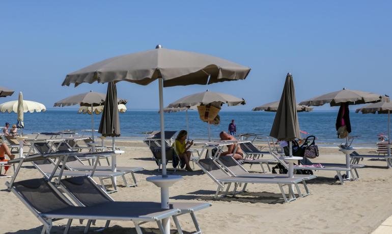 Spiaggia con ombrelloni grigi, sedie a sdraio e persone che si rilassano.