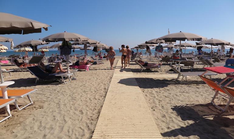 Spiaggia affollata con ombrelloni e lettini sotto un cielo sereno.