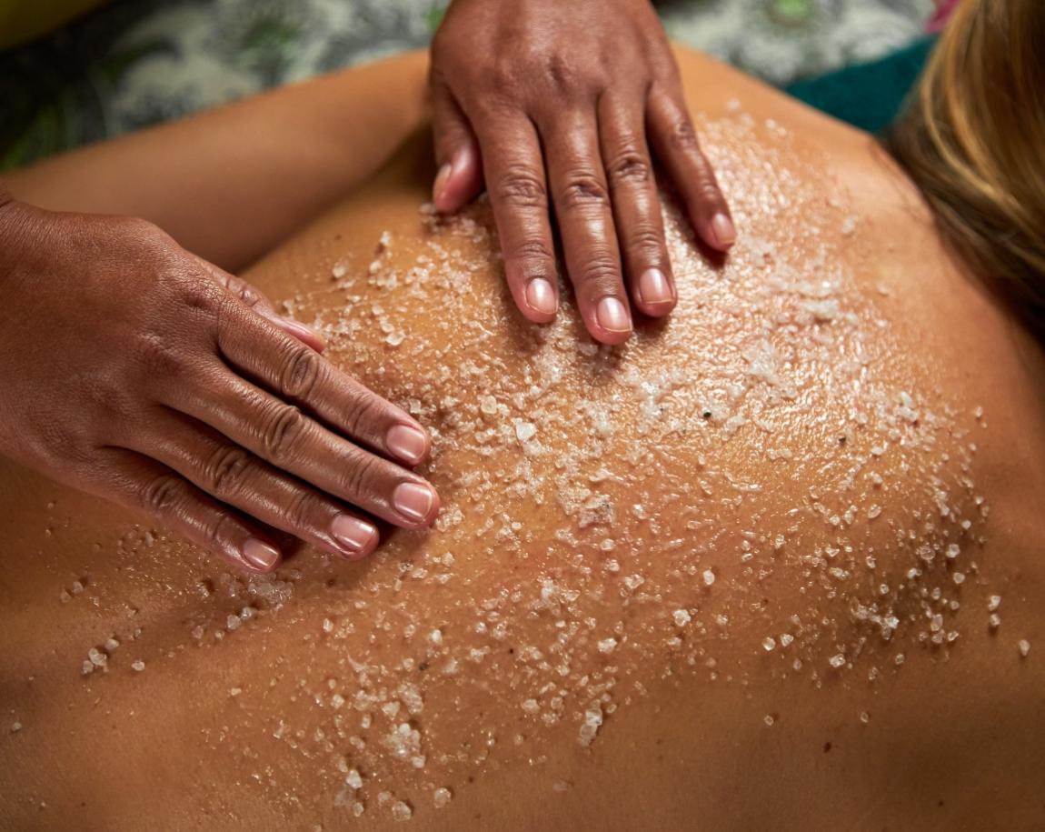 Massaggio esfoliante con sale su schiena per rimuovere cellule morte e rigenerare pelle.