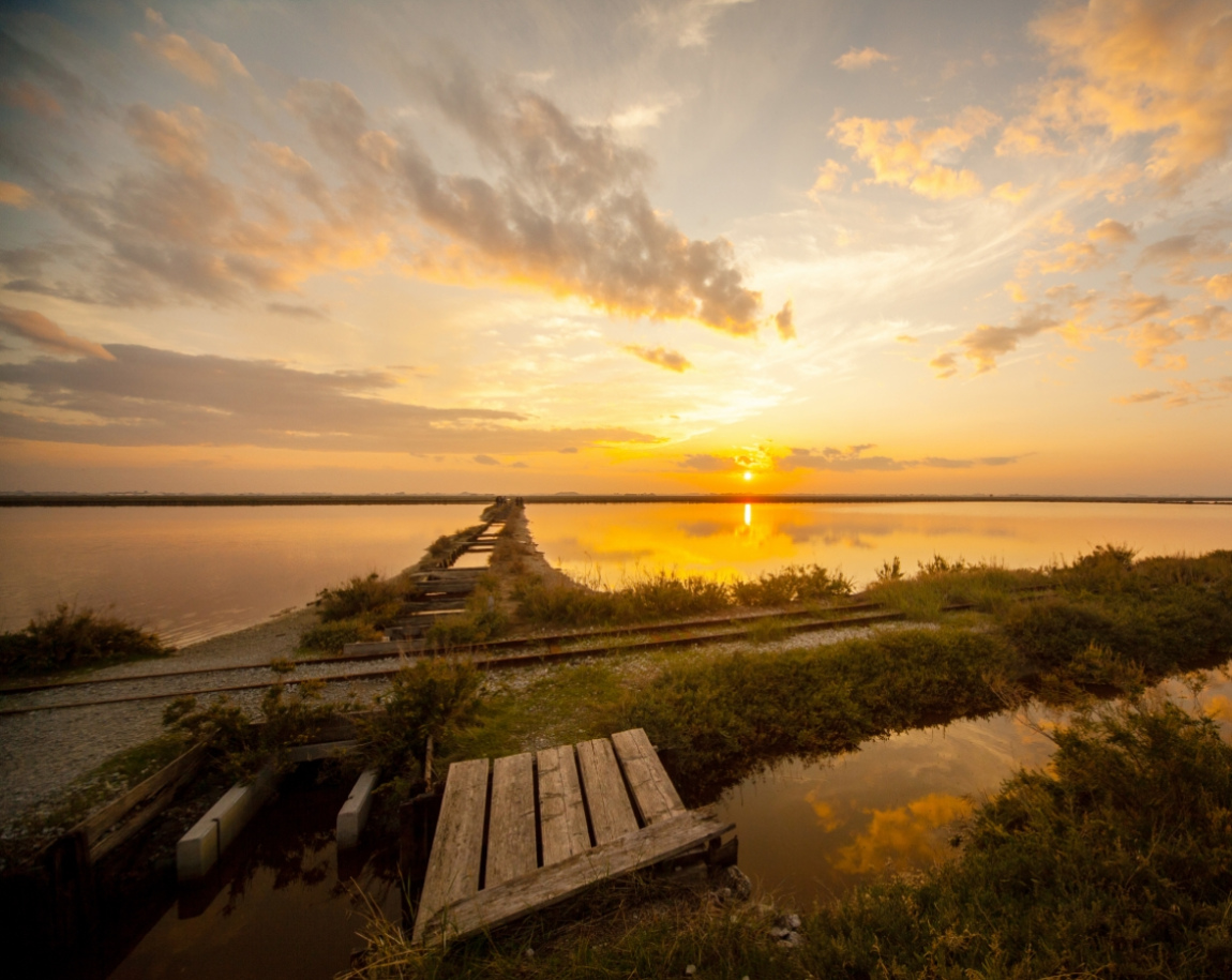 Tramonto su un lago con passerella di legno e riflessi dorati.