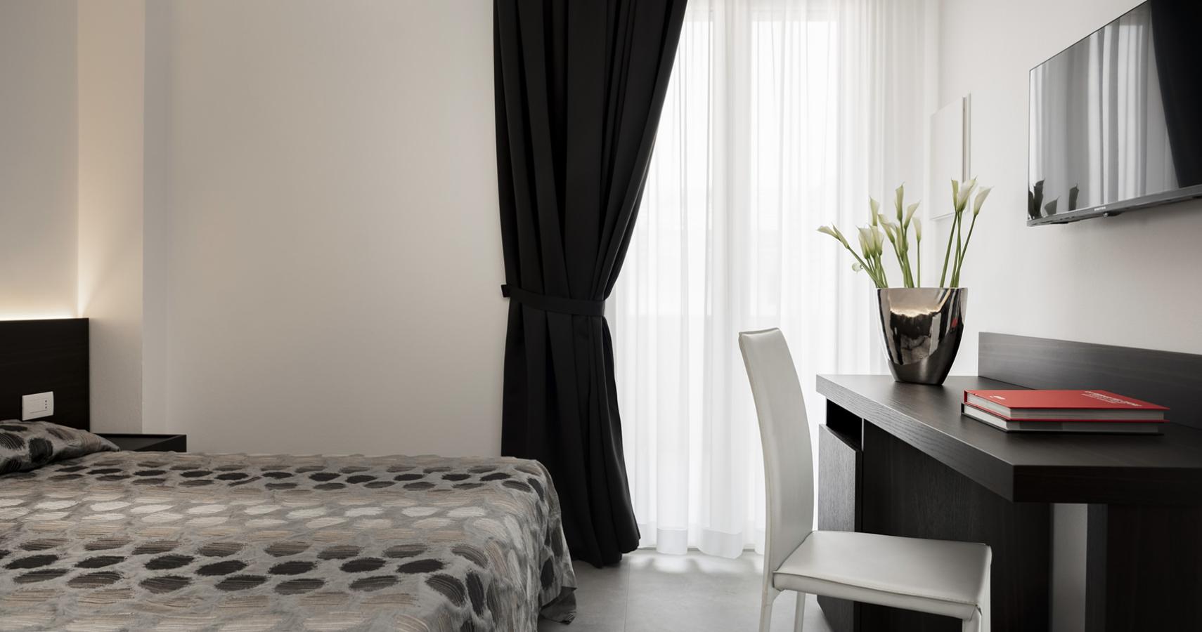 Camera moderna con letto accogliente, scrivania elegante e tende scure.
