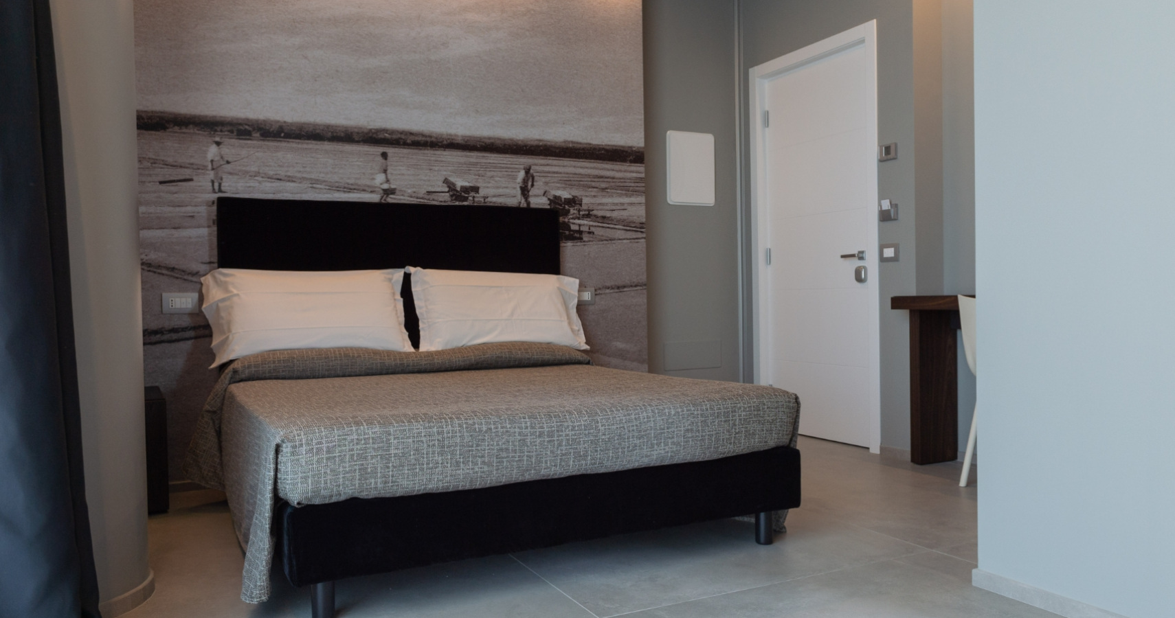 Camera moderna con letto matrimoniale, parete decorativa e arredo minimale.