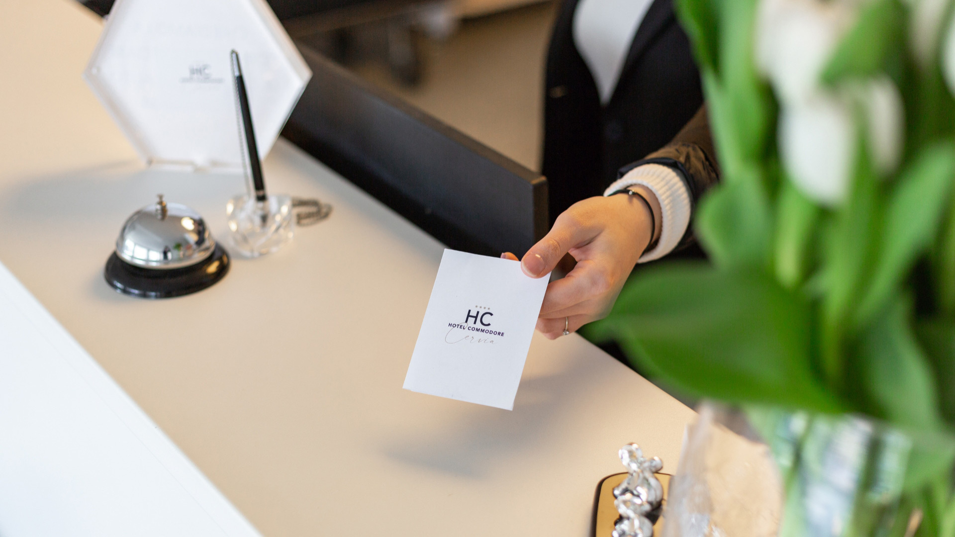 Reception di un hotel con campanello e documento 'Hotel Commodore Cervia'.
