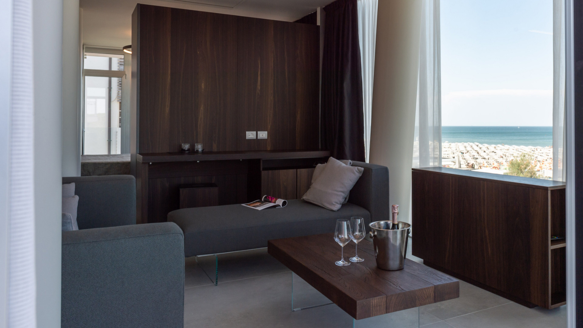 Soggiorno moderno con vista mare, divano grigio e tavolino in legno.