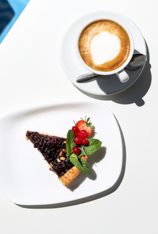 Cappuccino con cuore e crostata ai frutti di bosco su piatto bianco.