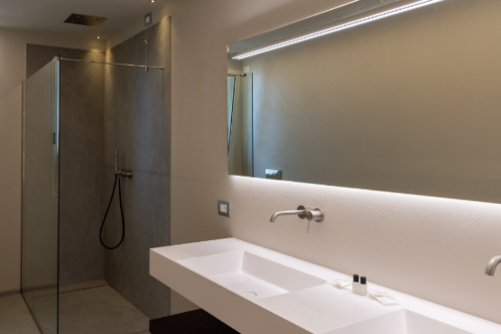 Bagno moderno con doccia in vetro, lavabo bianco e specchio illuminato.