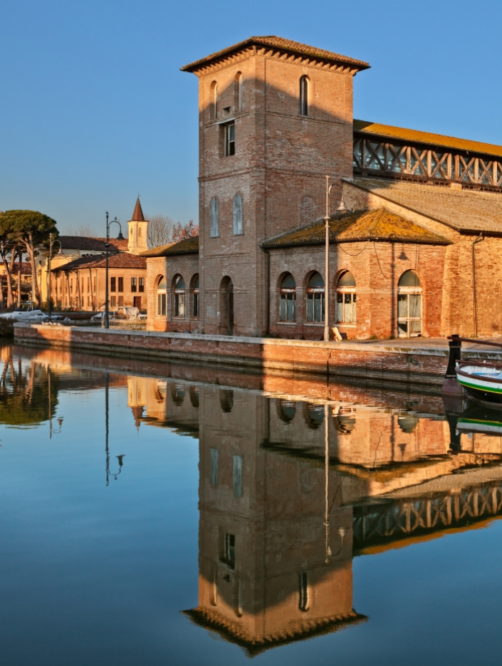 Edificio storico riflesso nell'acqua, architettura in mattoni, atmosfera serena.