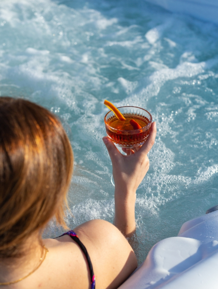 Persona in jacuzzi con cocktail, guarnito con scorza d'arancia, in mano.
