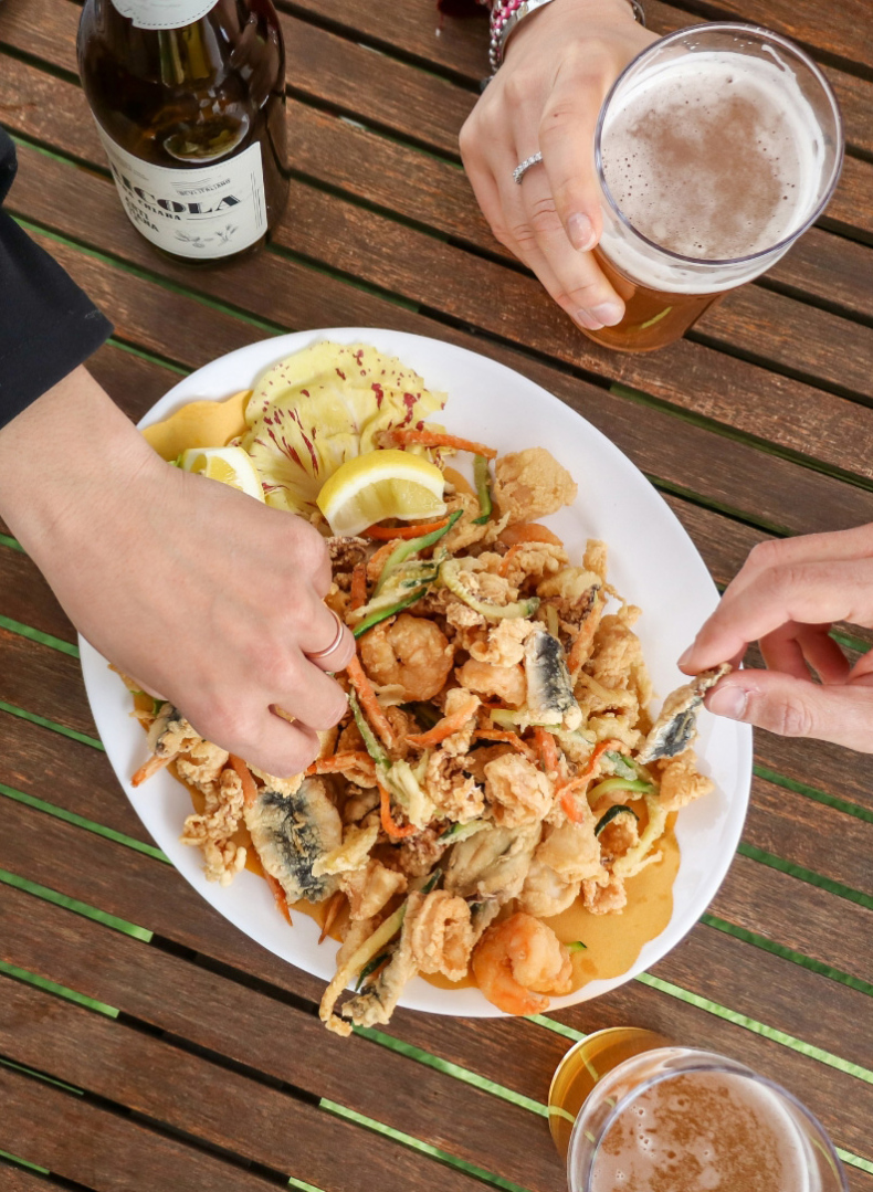 Persone condividono un piatto di fritto misto con birra su un tavolo di legno.