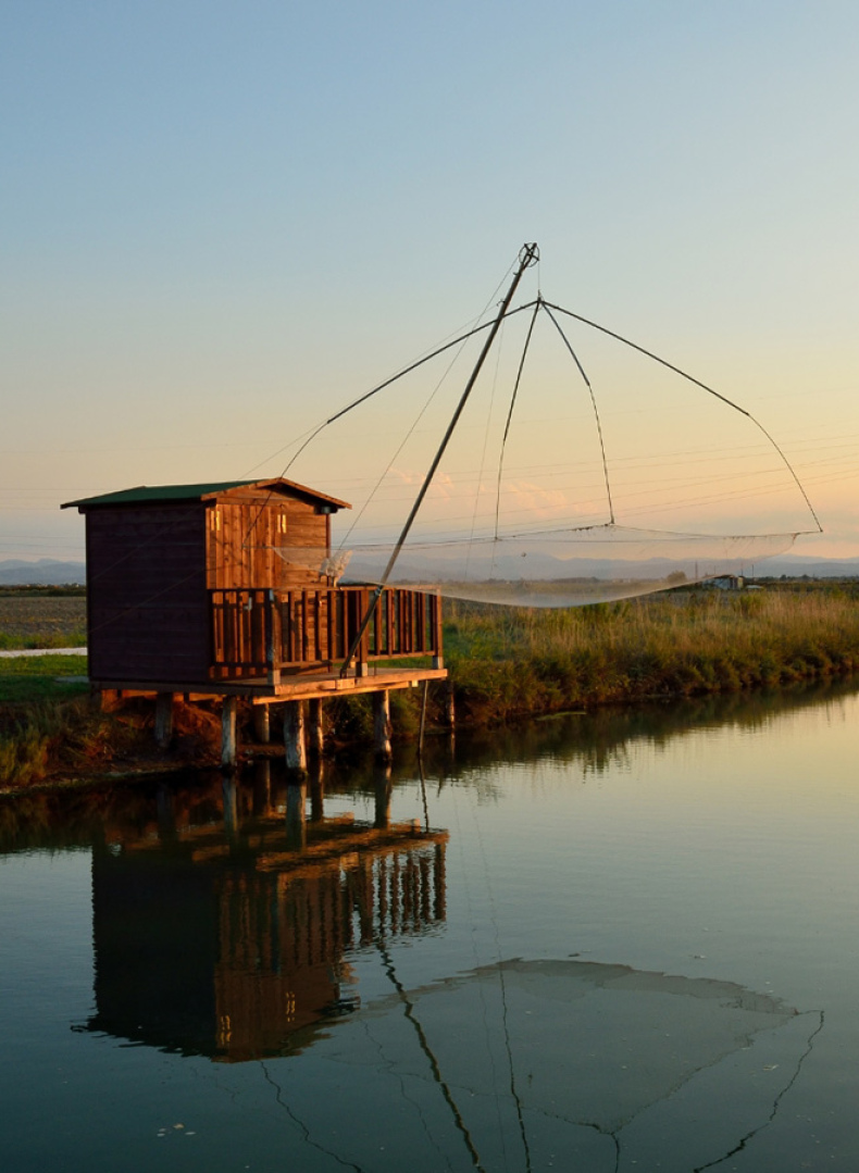 Capanno da pesca su un canale al tramonto, riflesso nell'acqua calma.