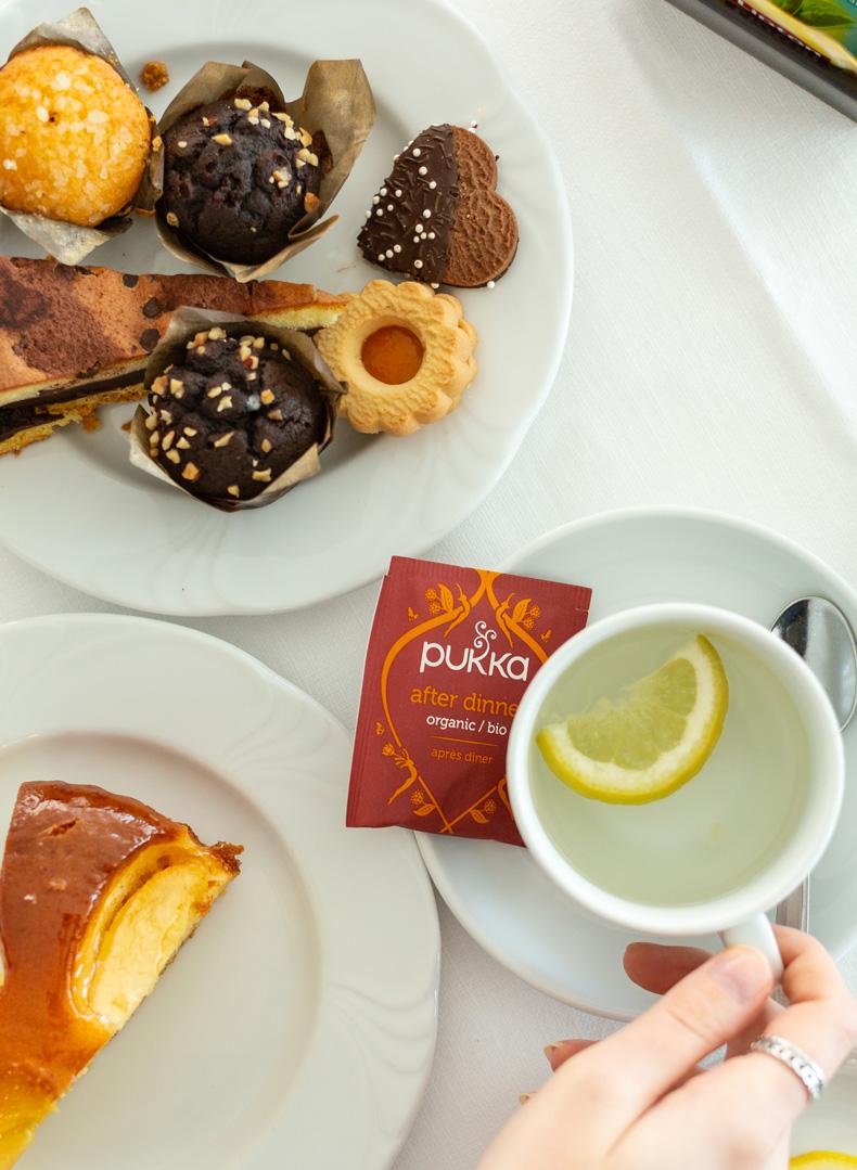 Dolci assortiti con tè al limone e infuso biologico Pukka su tavola bianca.