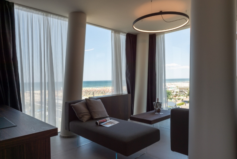 Salotto moderno con vista mare, chaise longue e tavolino, luce naturale.