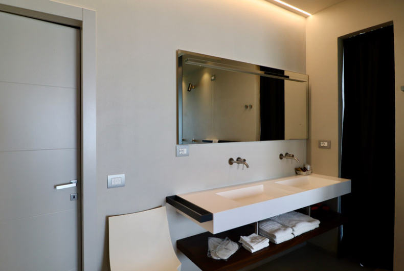 Bagno moderno con lavandino doppio, specchio grande e asciugamani riposti sotto.
