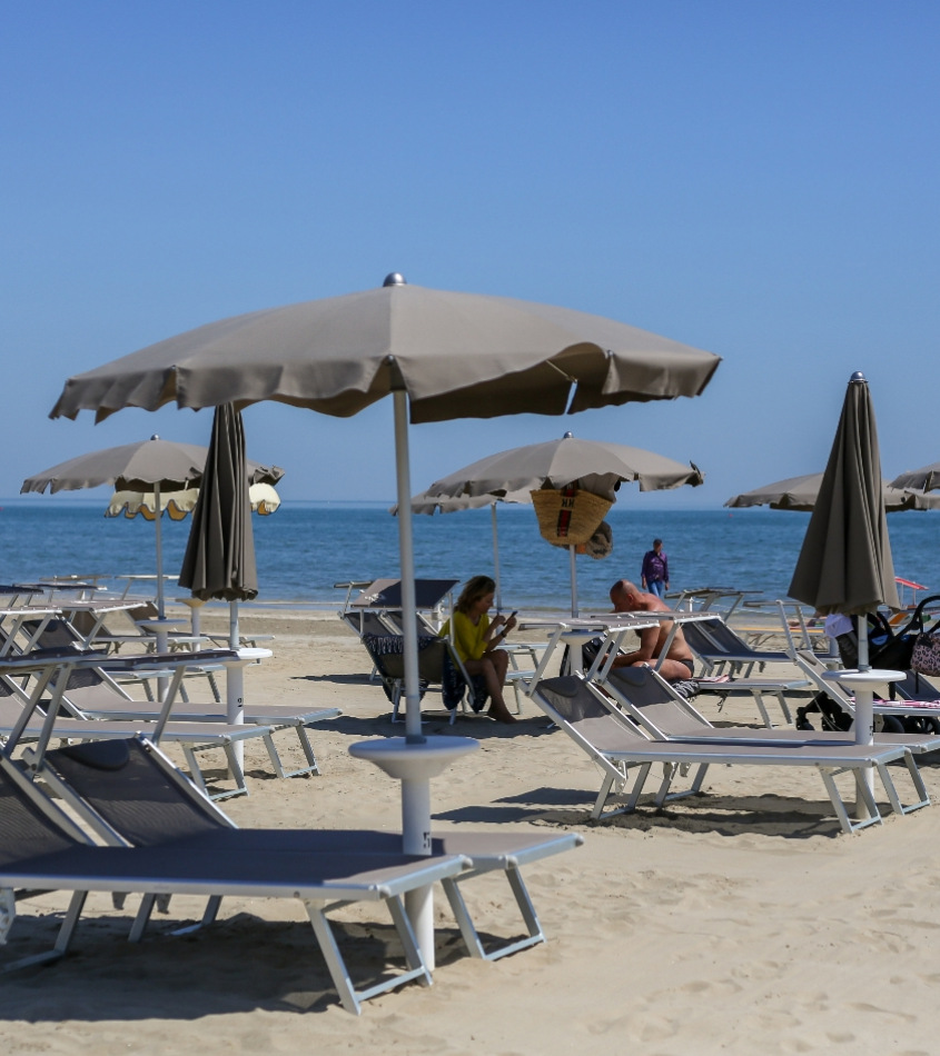Spiaggia con ombrelloni grigi e lettini, persone rilassate sotto il sole.