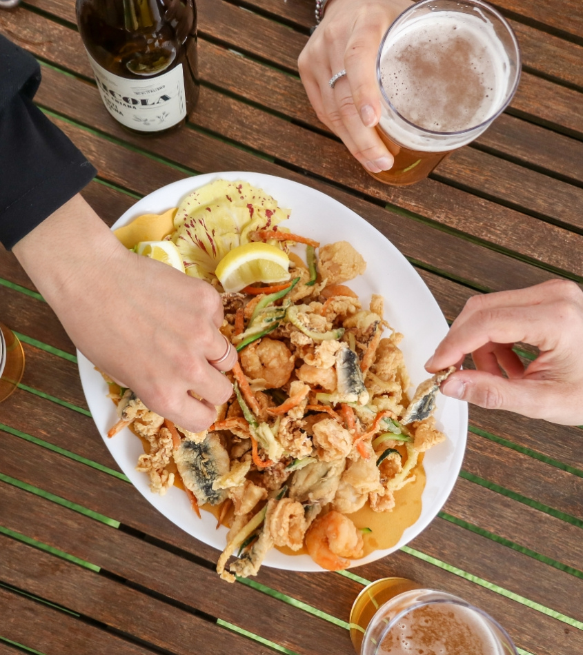 Piatto di fritto misto con birra su tavolo di legno, mani che prendono cibo.